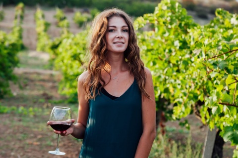 Mulher entre vinhedos com uma taça de vinho na mão  
