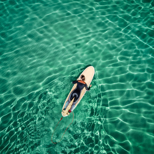 
			Un surfeur rame dans la mer
		