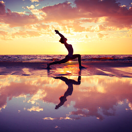 Frau praktiziert Yoga bei Sonnenuntergang am Strand