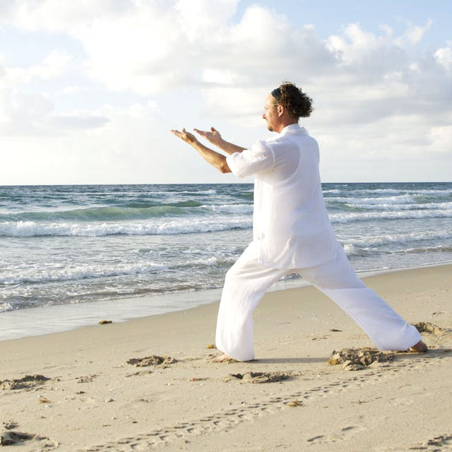 Hombre practicando yoga en la playa 